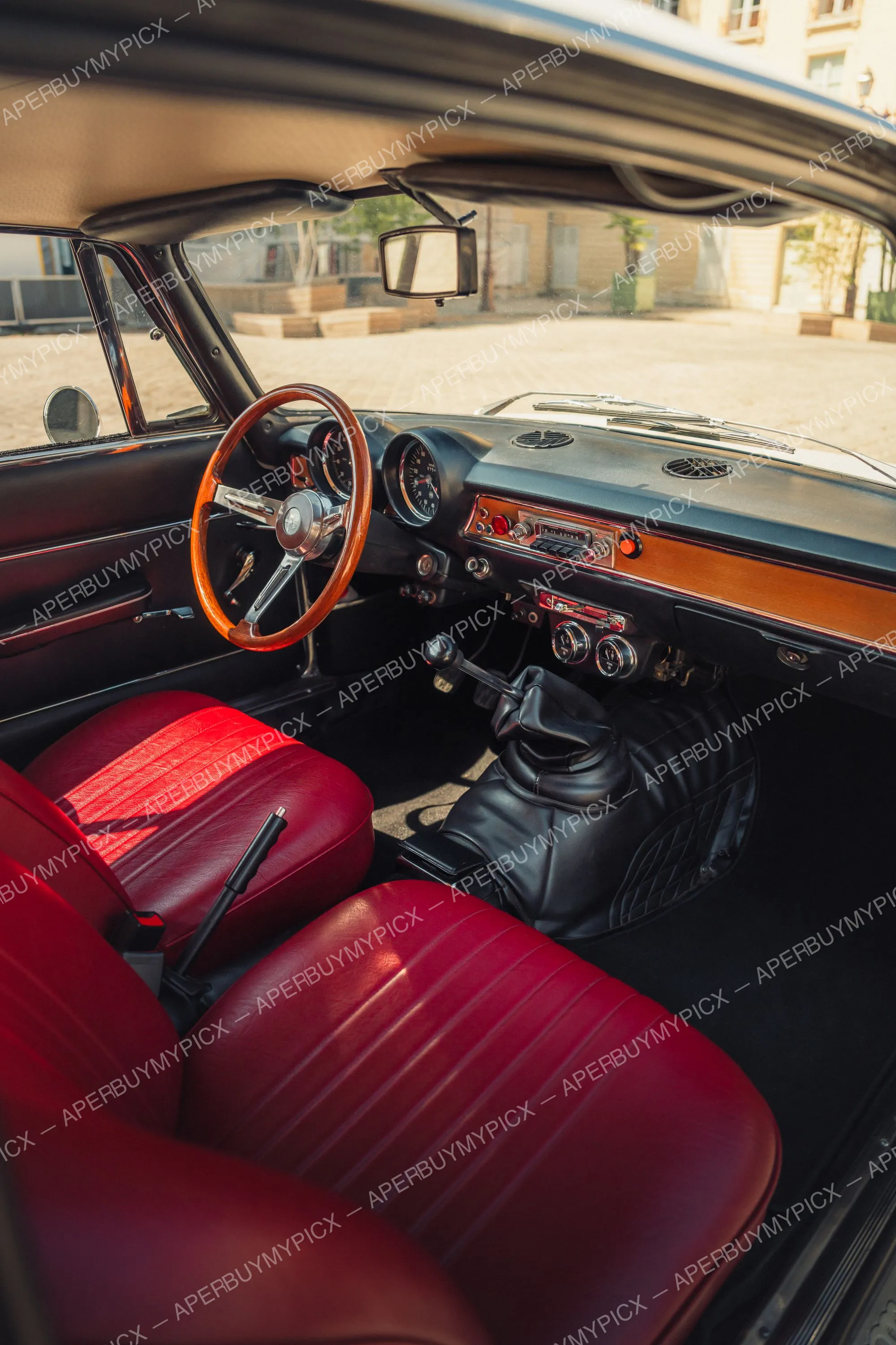 Intérieur d'une Alfa Romeo 1600 vintage avec sièges en cuir rouge, volant en bois, tableau de bord en bois et compteurs classiques, levier de vitesse manuel