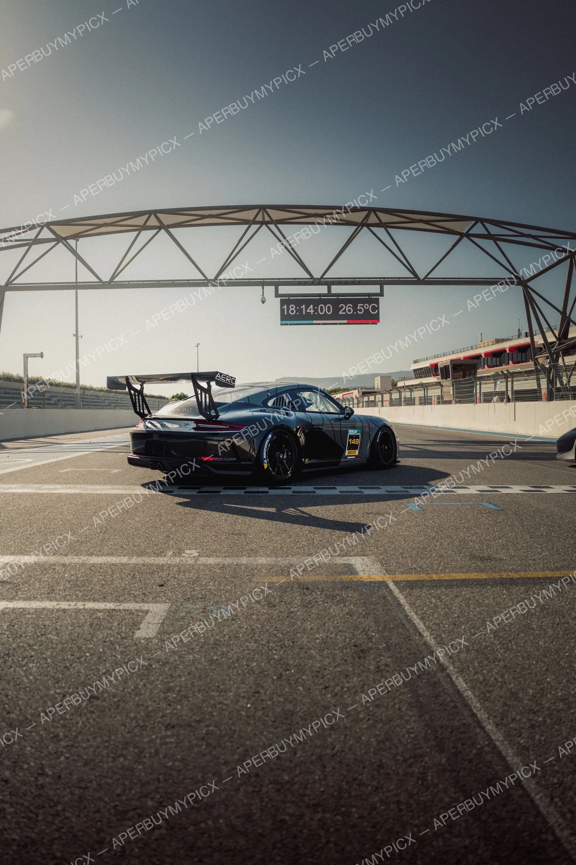 Porsche 911 GT3 Cup noire numéro 149 arrêtée sur la voie des stands du circuit Paul Ricard au Castellet, sous le portique affichant 18:14 et 26,5°C.