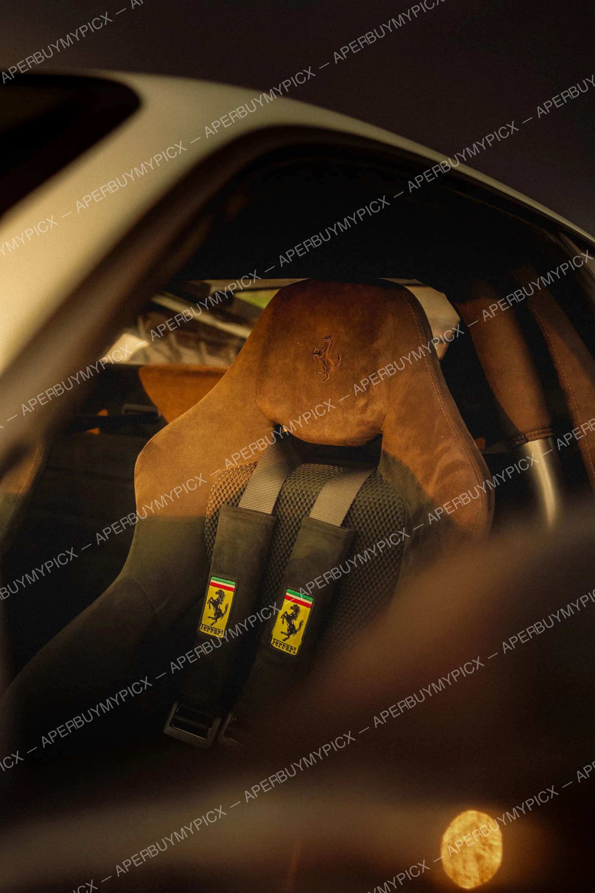 Siège baquet Ferrari en alcantara marron avec logo cheval cabré et harnais quatre points aux écussons Ferrari jaunes, vu à travers la vitre d'une voiture de sport dans une lumière chaude
