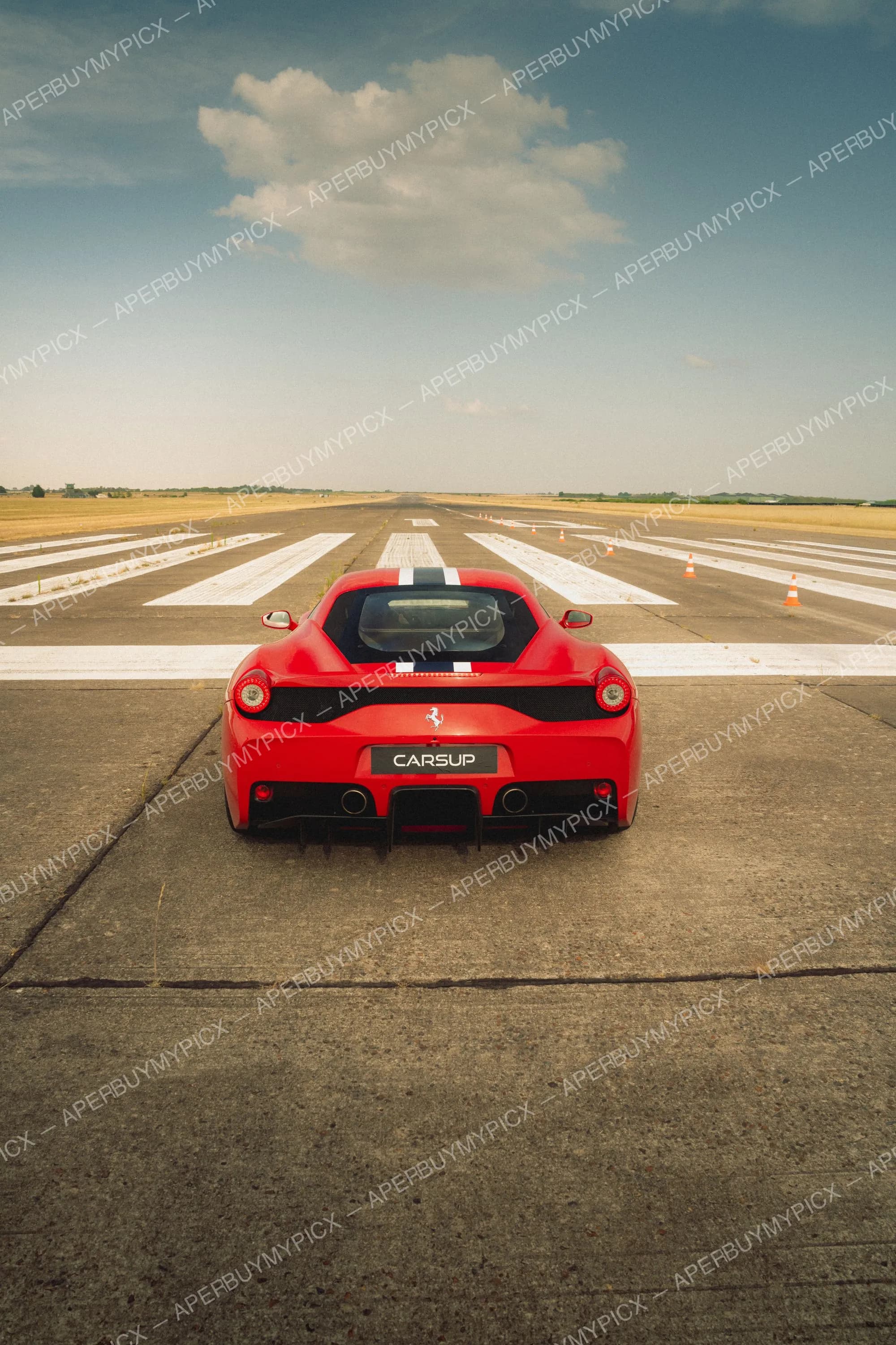 Ferrari 458 Speciale rouge vue de l'arrière sur une piste d'aéroport, bandes blanches, cônes orange et ciel bleu nuageux à l'horizon