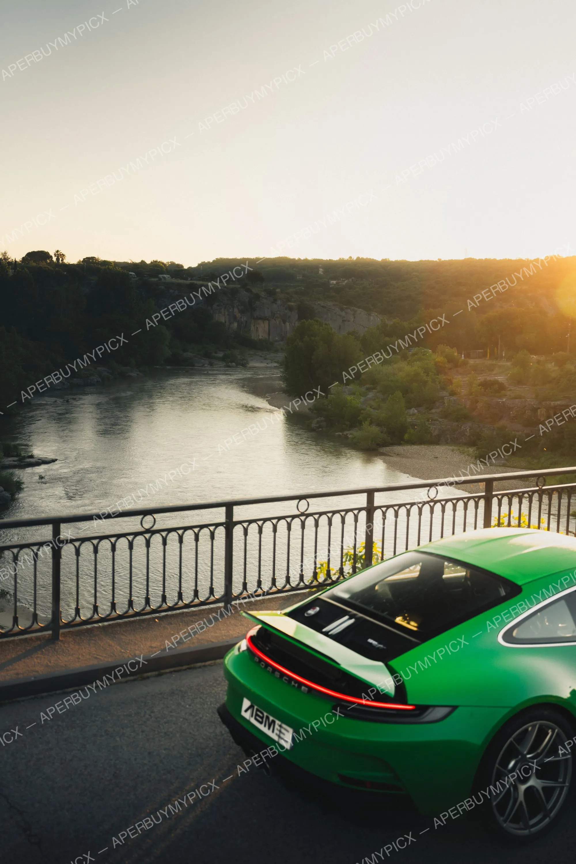 Porsche 911 (992) ST verte vue de l'arrière, garée sur un pont surplombant une rivière entourée de collines boisées au coucher du soleil