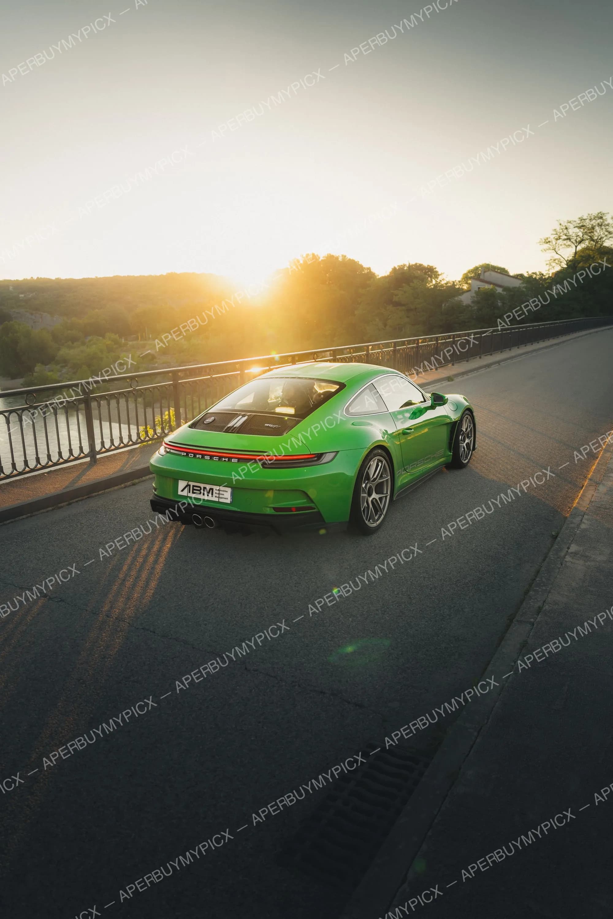Porsche 911 992 ST verte vue de trois quarts arrière sur un pont au coucher du soleil, jantes argentées et diffuseur noir