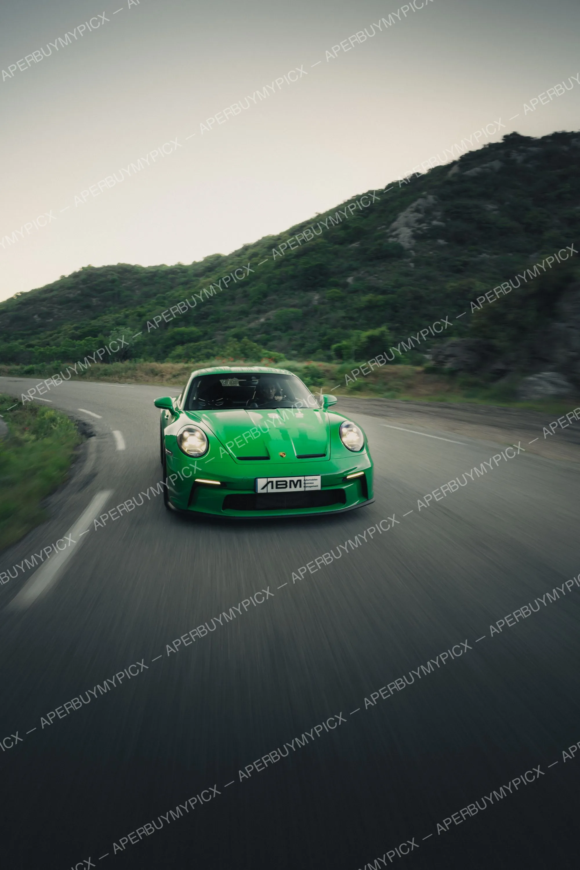Porsche 911 GT3 verte roulant à vive allure sur une route de montagne sinueuse au crépuscule