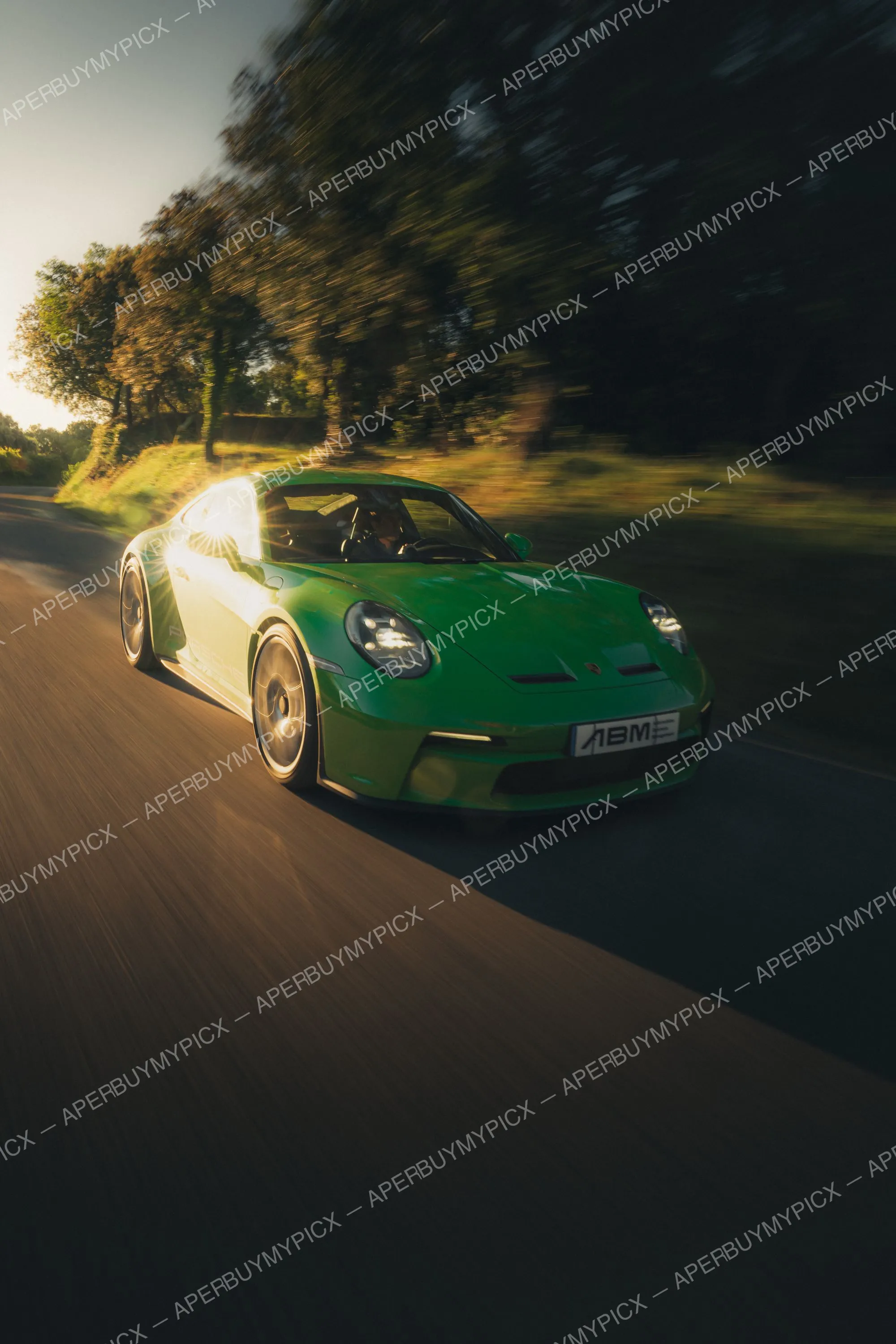 Porsche 911 (992) ST vert vif roulant à vive allure sur une route de campagne au coucher du soleil, effet de filé et reflet solaire