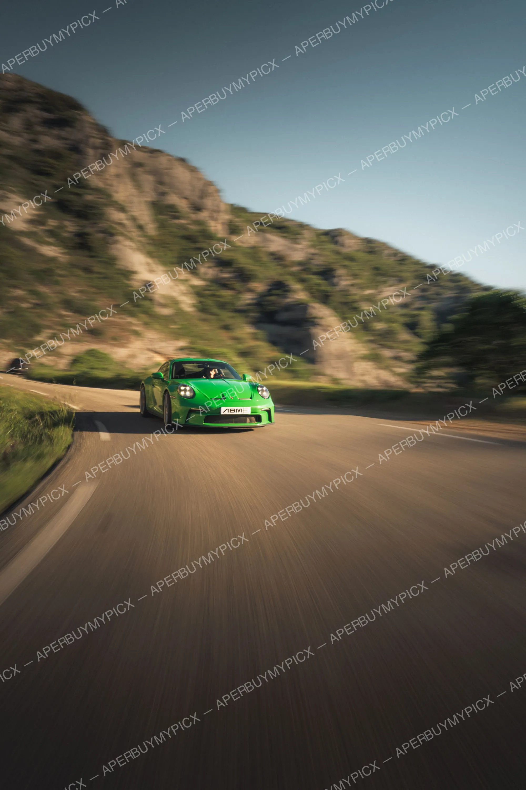 Porsche 911 992 ST verte roulant à vive allure sur une route de montagne sinueuse au coucher du soleil, effet de filé