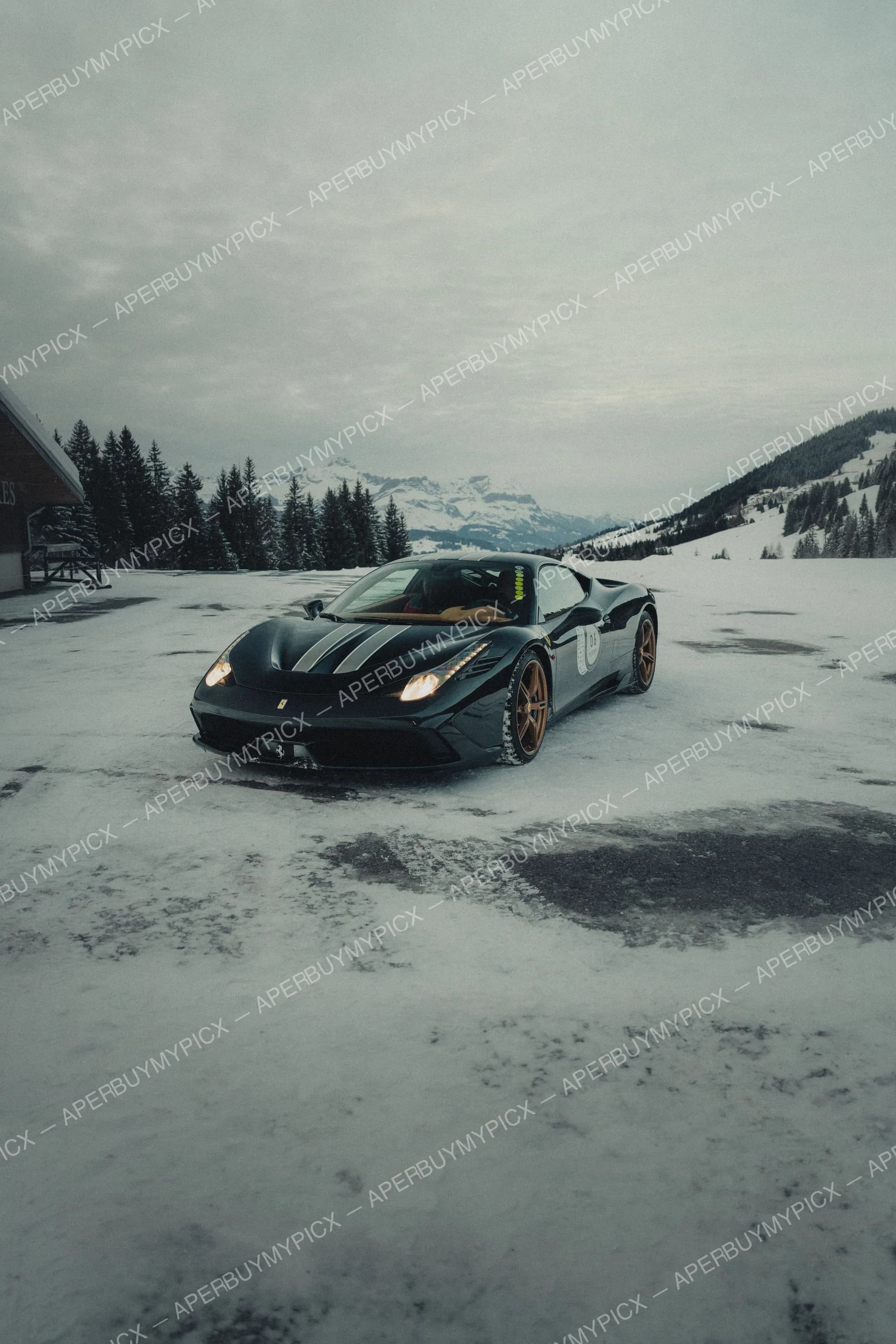 Ferrari 458 Speciale noire à bande centrale et jantes bronze garée sur la neige devant les montagnes alpines enneigées de Megève sous un ciel nuageux