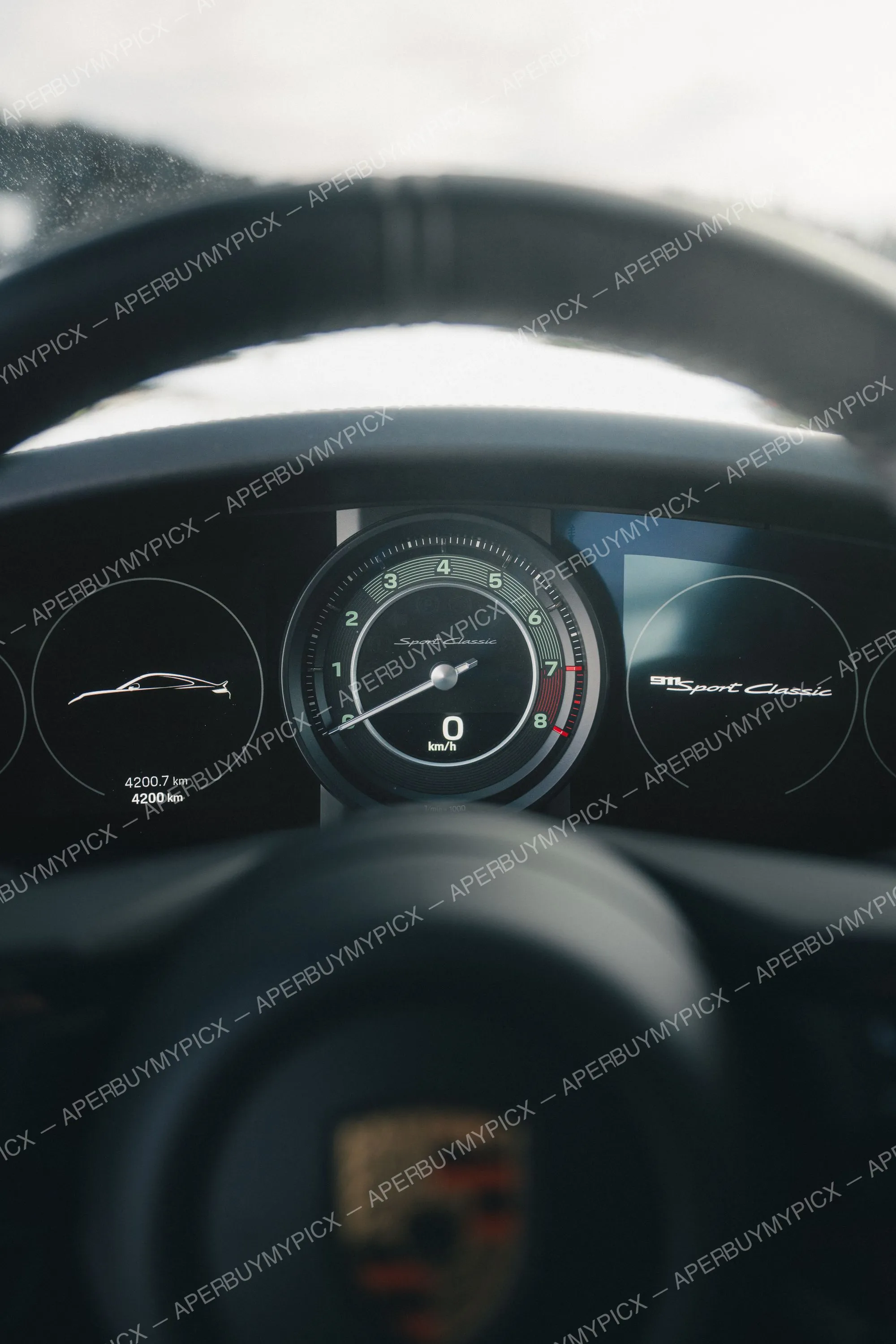 Tableau de bord d'une Porsche 911 Sport Classic vu à travers le volant, affichant le compte-tours numérique à 0 km/h et 4200 km au compteur.