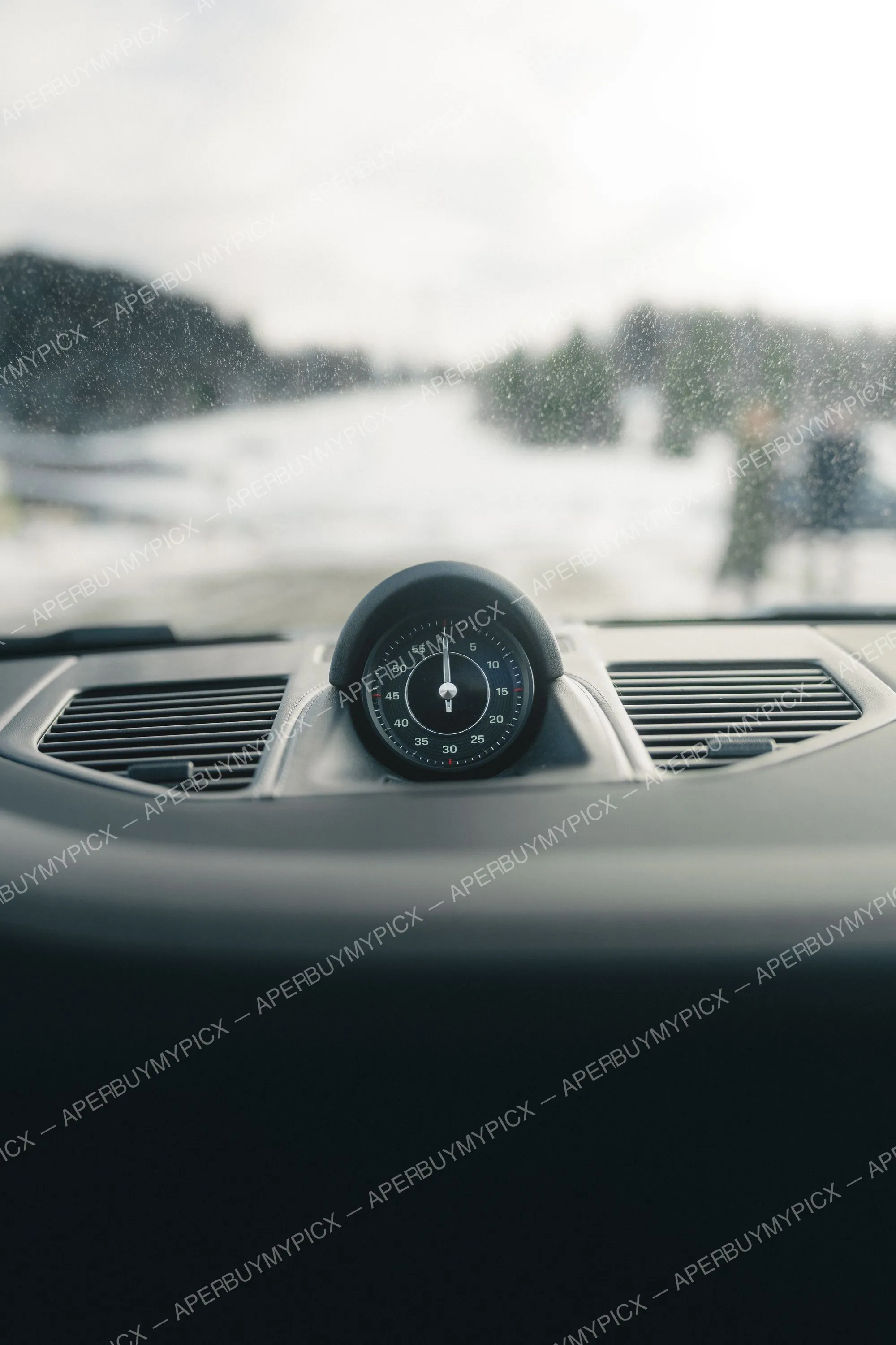Gros plan sur l'horloge chronographe du tableau de bord d'une voiture sport, avec un paysage enneigé et flou de Megève visible à travers le pare-brise