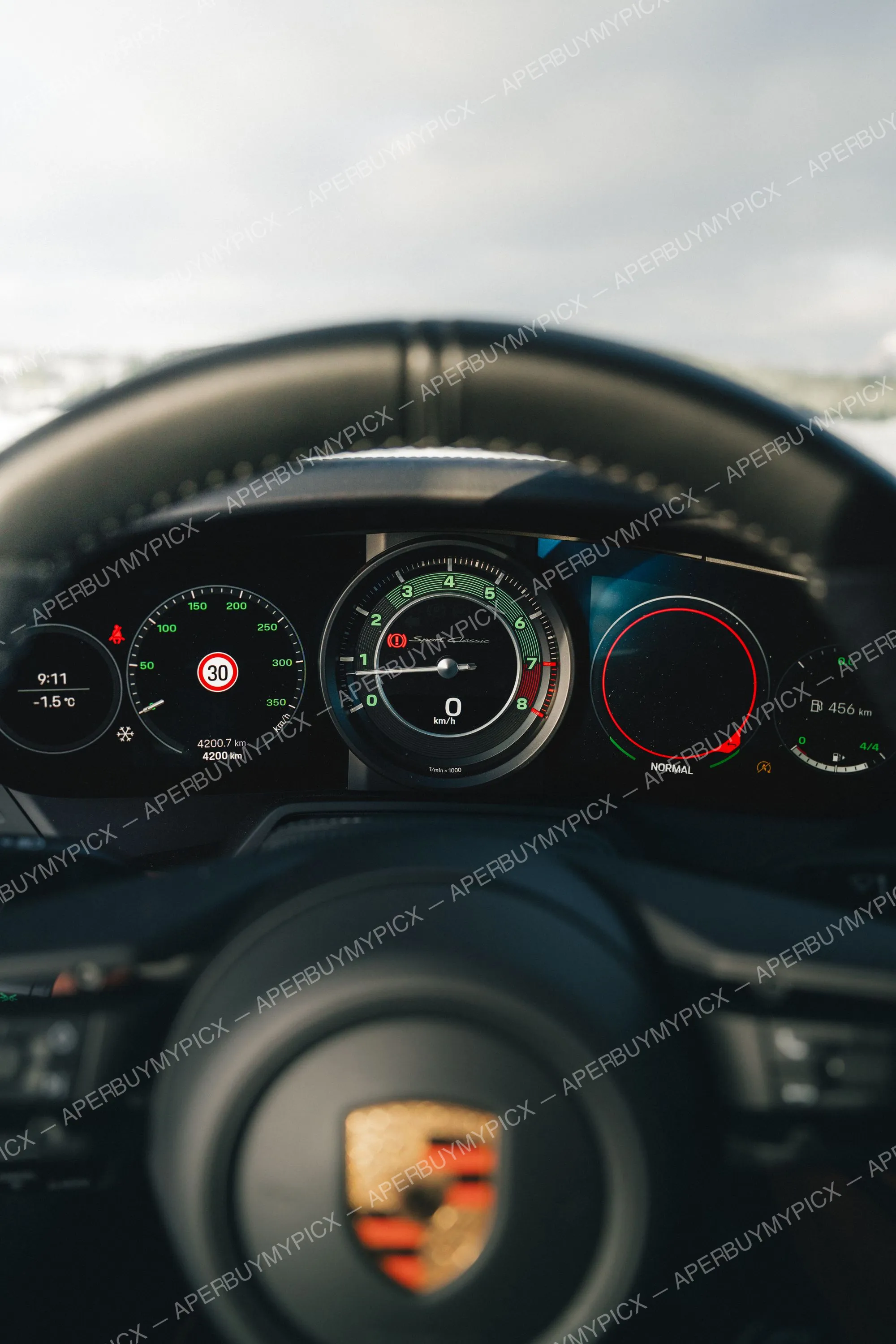 Tableau de bord numérique d'une Porsche 911 Sport Classic affichant 0 km/h, compte-tours, 9h11 et -1,5°C, mode Normal, vu à travers le volant avec logo Porsche.