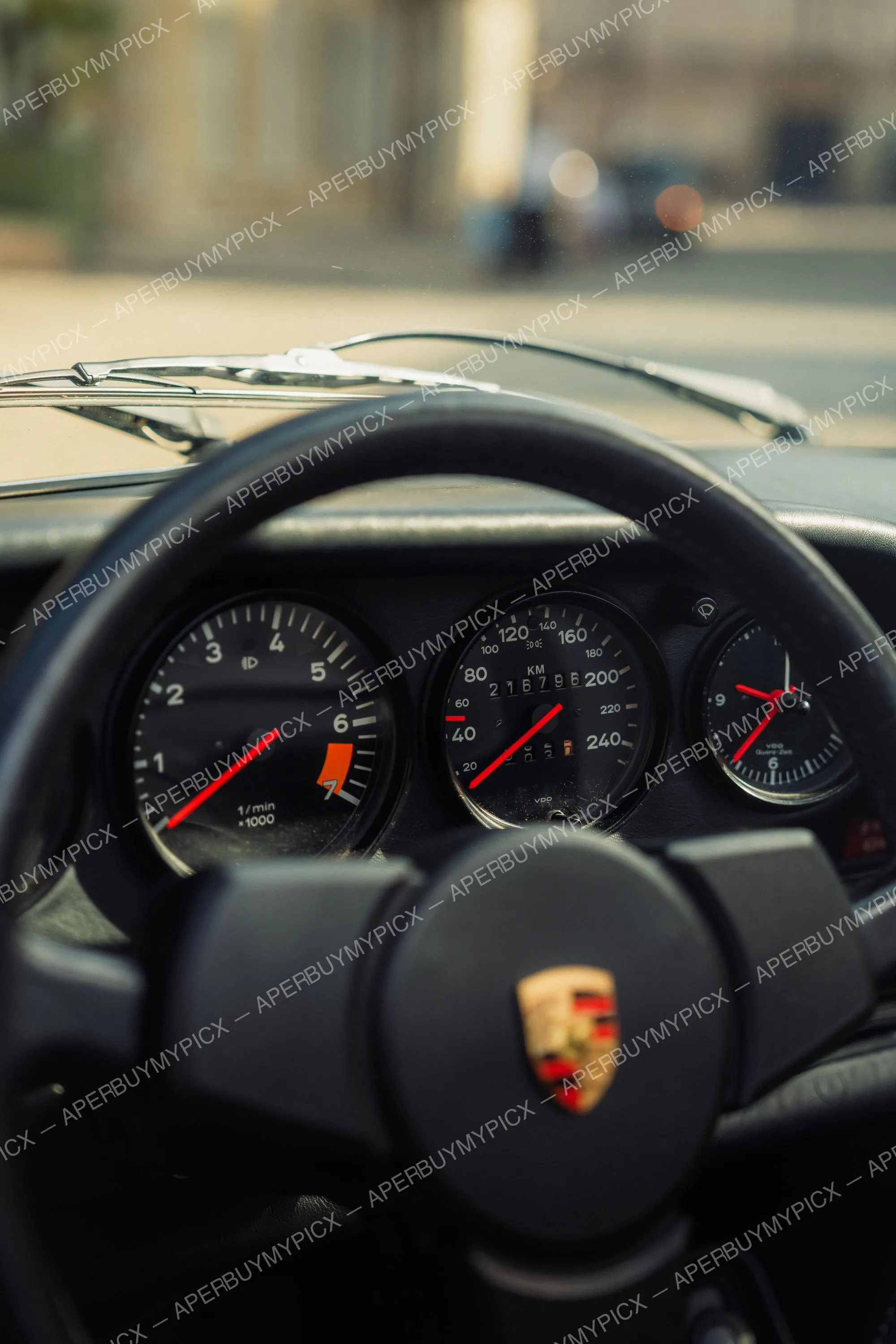Gros plan sur le tableau de bord d'une Porsche 911 SC Targa vintage, montrant le compte-tours, le compteur de vitesse affichant 216 796 km, l'horloge et le volant noir orné du logo Porsche.