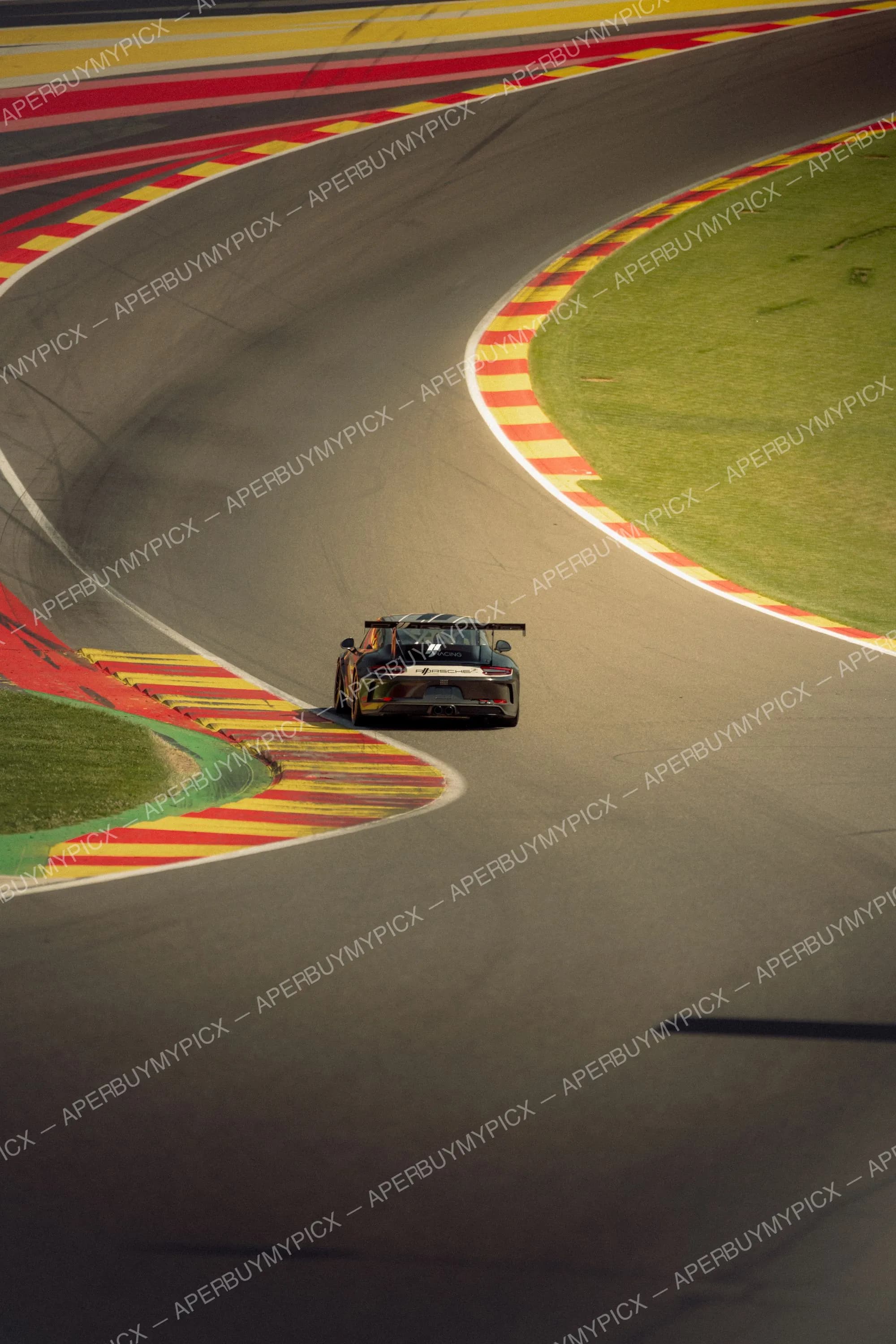 Porsche 911 GT3 Cup noire abordant une chicane sur le circuit de Spa-Francorchamps, entourée de vibreurs rouge et jaune et de zones herbeuses vertes