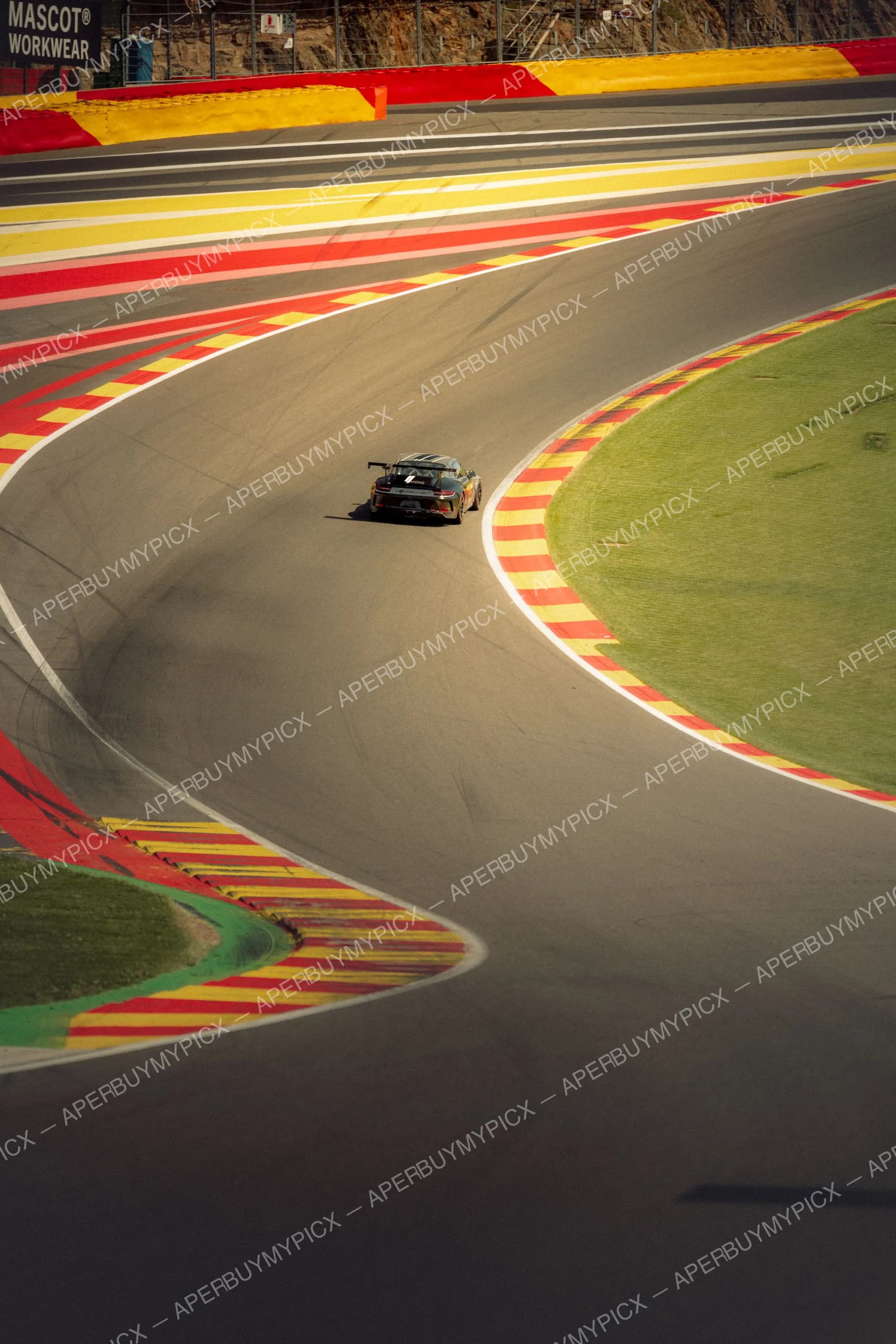 Une Porsche 911 GT3 Cup noire aborde un virage sinueux du circuit de Spa-Francorchamps, entourée des vibreurs rouges et jaunes caractéristiques et de bordures gazonnées.