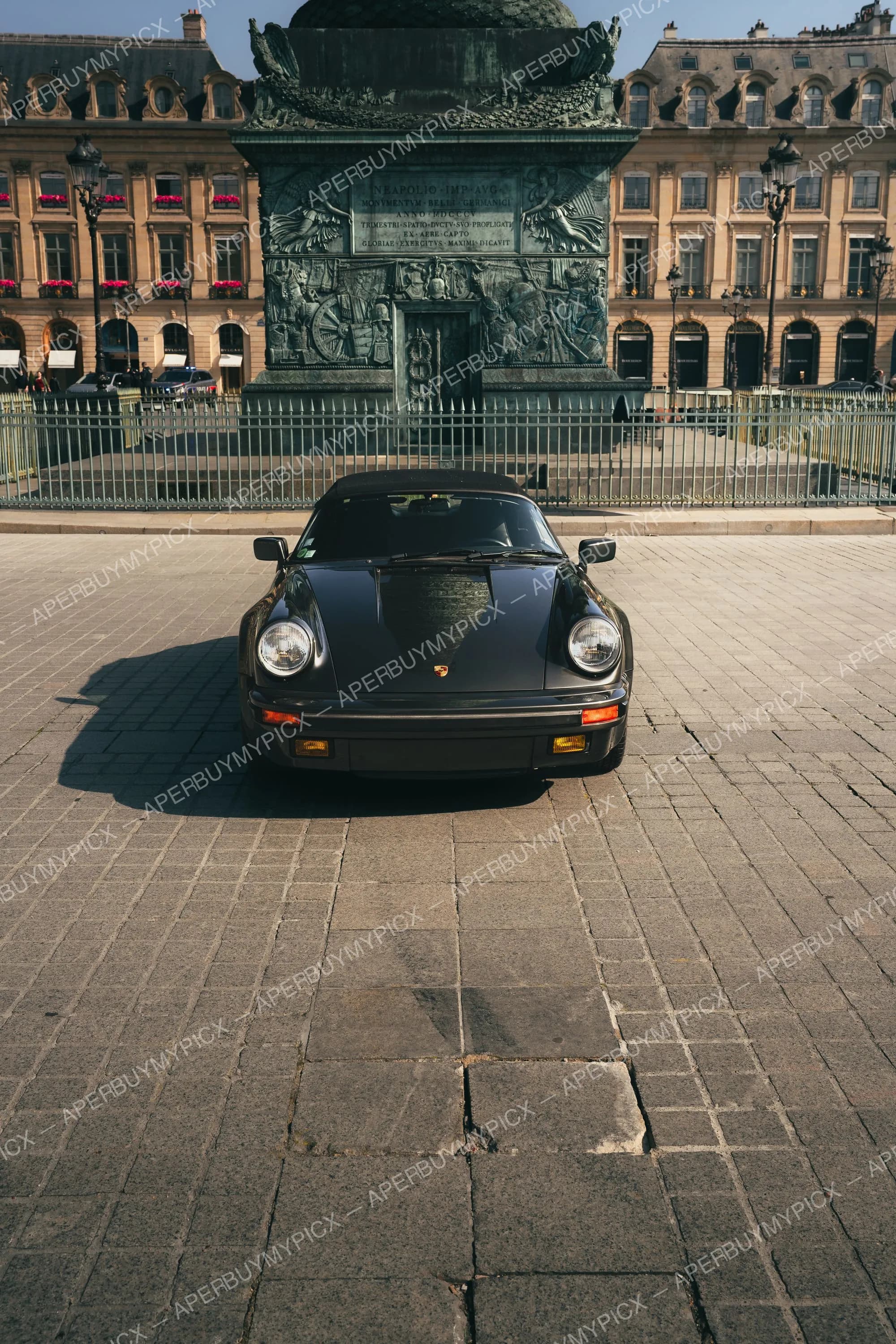 Porsche 911 Speedster noire décapotable garée sur les pavés de la Place Vendôme à Paris, devant la colonne Vendôme et les bâtiments haussmanniens en pierre.