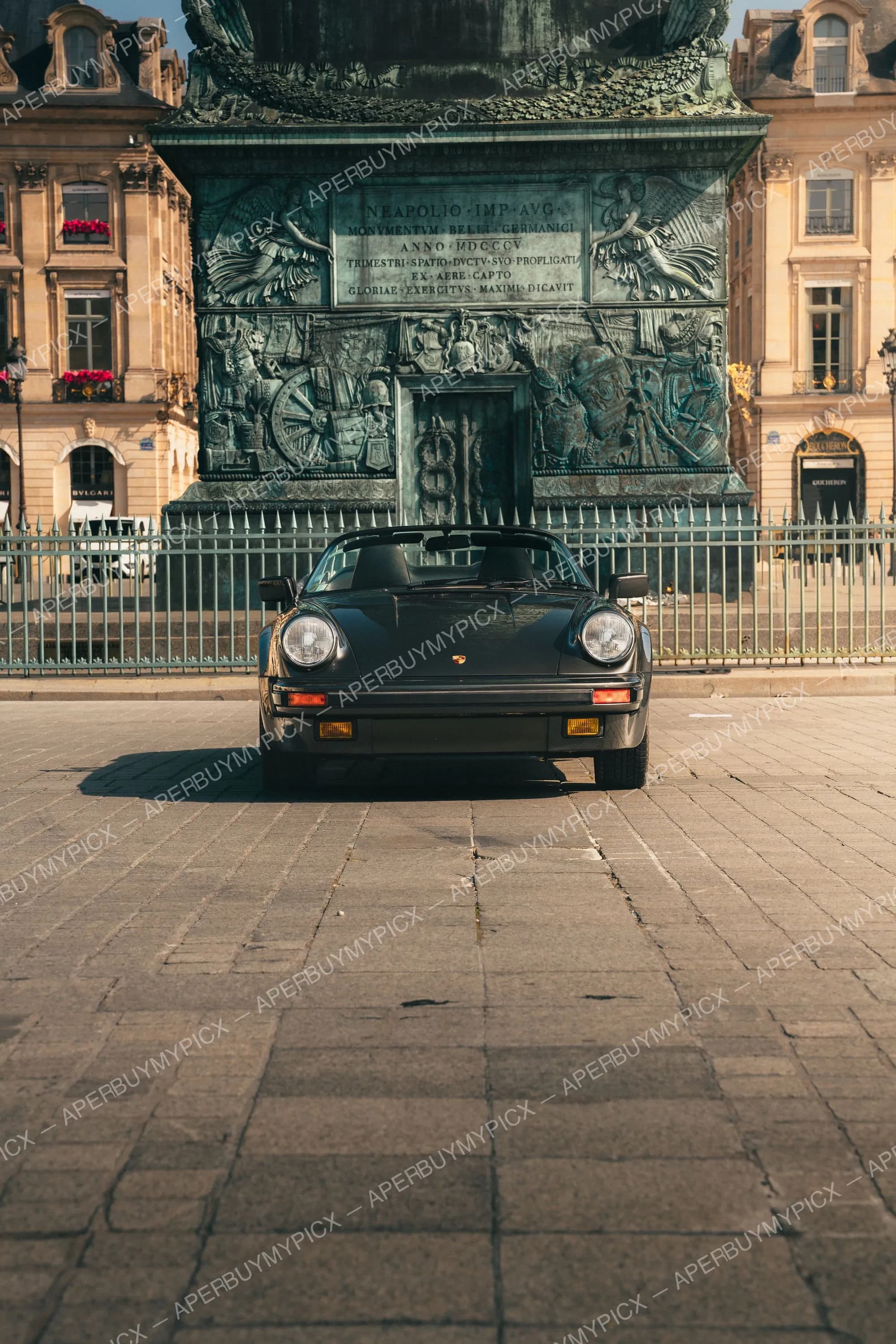 Porsche 911 Speedster noire vue de face, garée sur les pavés de la place Vendôme devant la colonne en bronze, entourée de bâtiments haussmanniens à Paris.