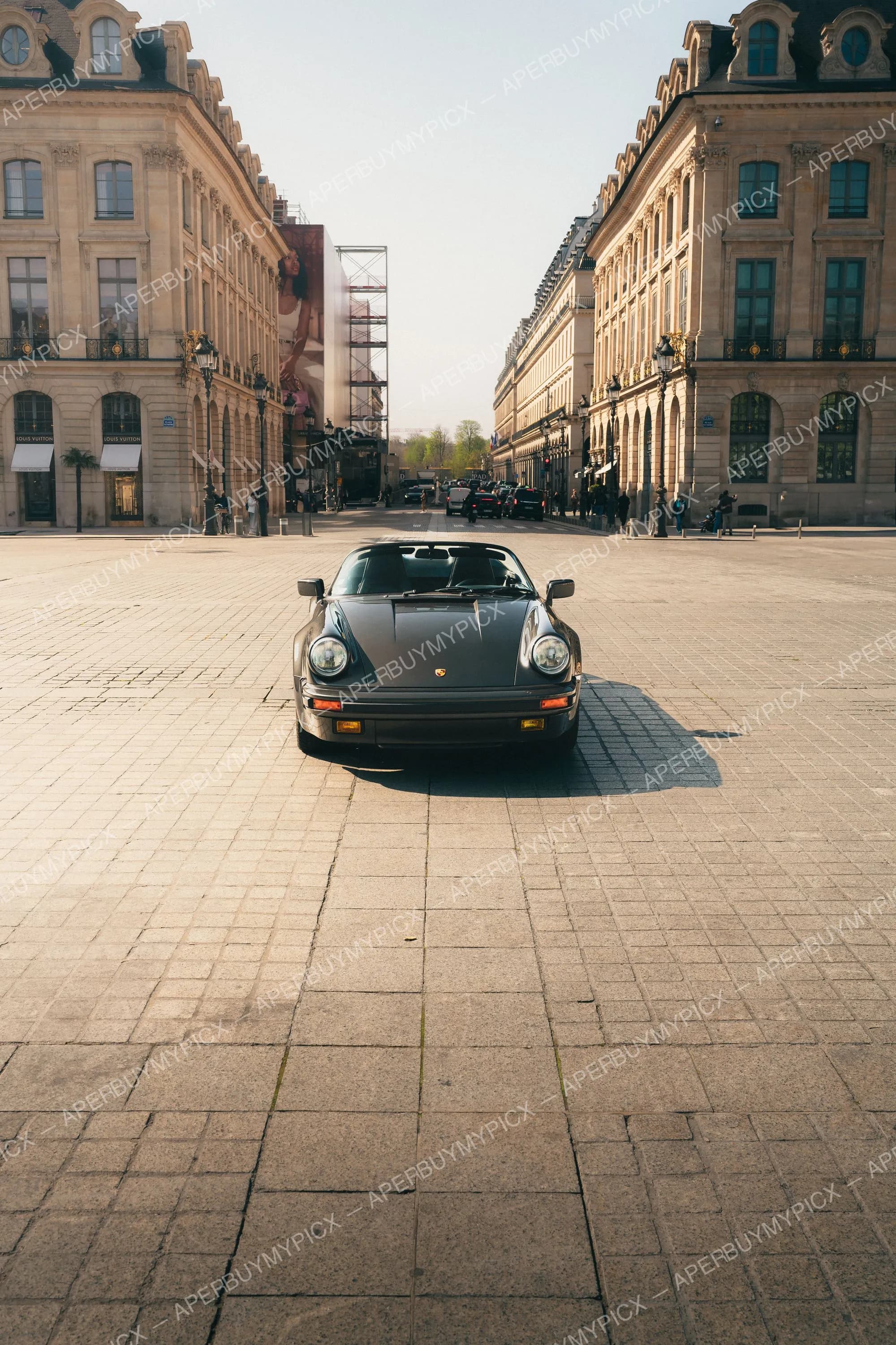 Porsche 911 Speedster noire garée au centre de la Place Vendôme à Paris, vue de face, entourée de bâtiments haussmanniens dorés à la lumière du matin.