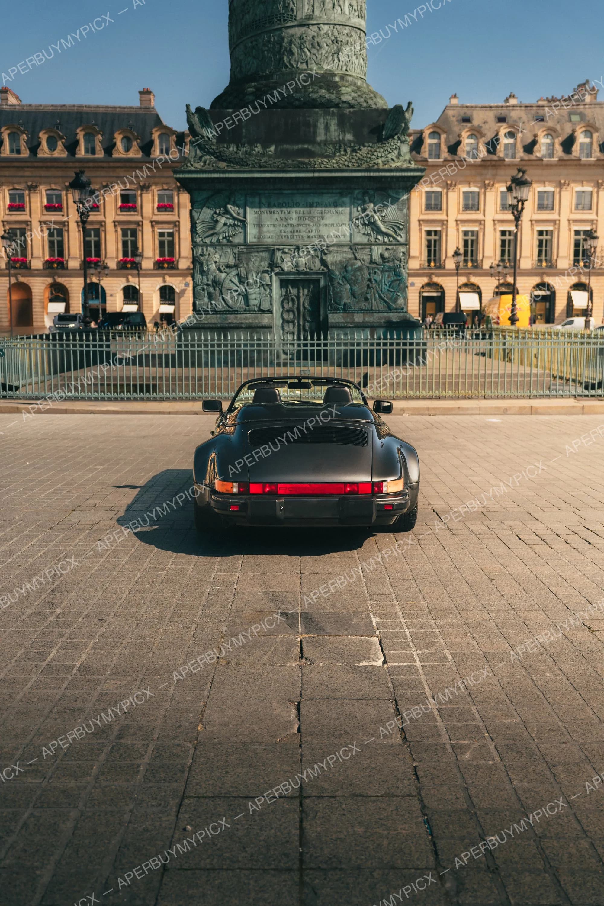 Porsche 911 Speedster noire vue de l'arrière, garée sur les pavés de la Place Vendôme à Paris, devant la colonne Vendôme et les façades haussmanniennes