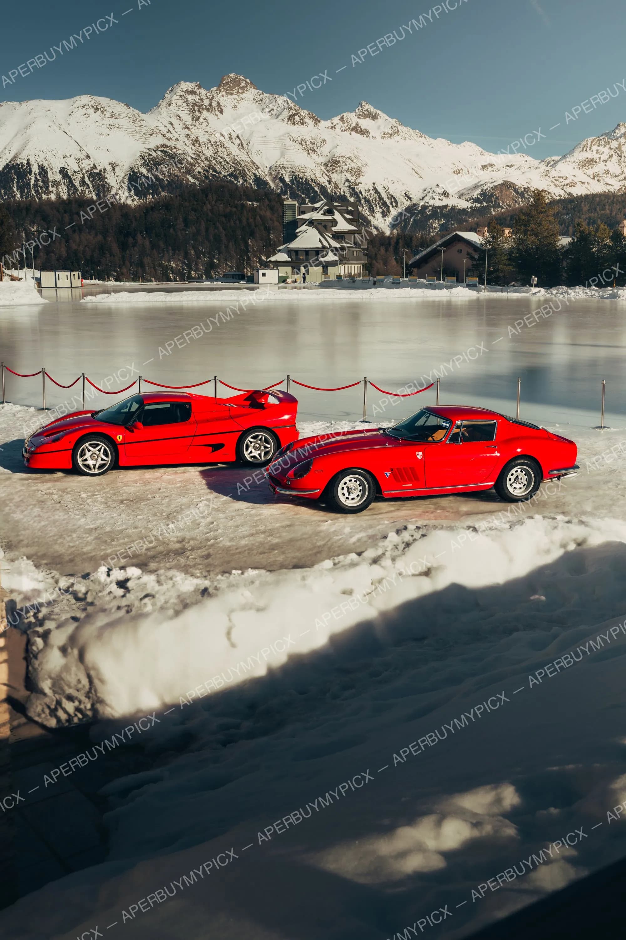 Deux Ferrari rouges, une F50 moderne et une 275 GTB classique, stationnées sur un lac gelé à St. Moritz avec des montagnes enneigées en arrière-plan sous un ciel bleu.