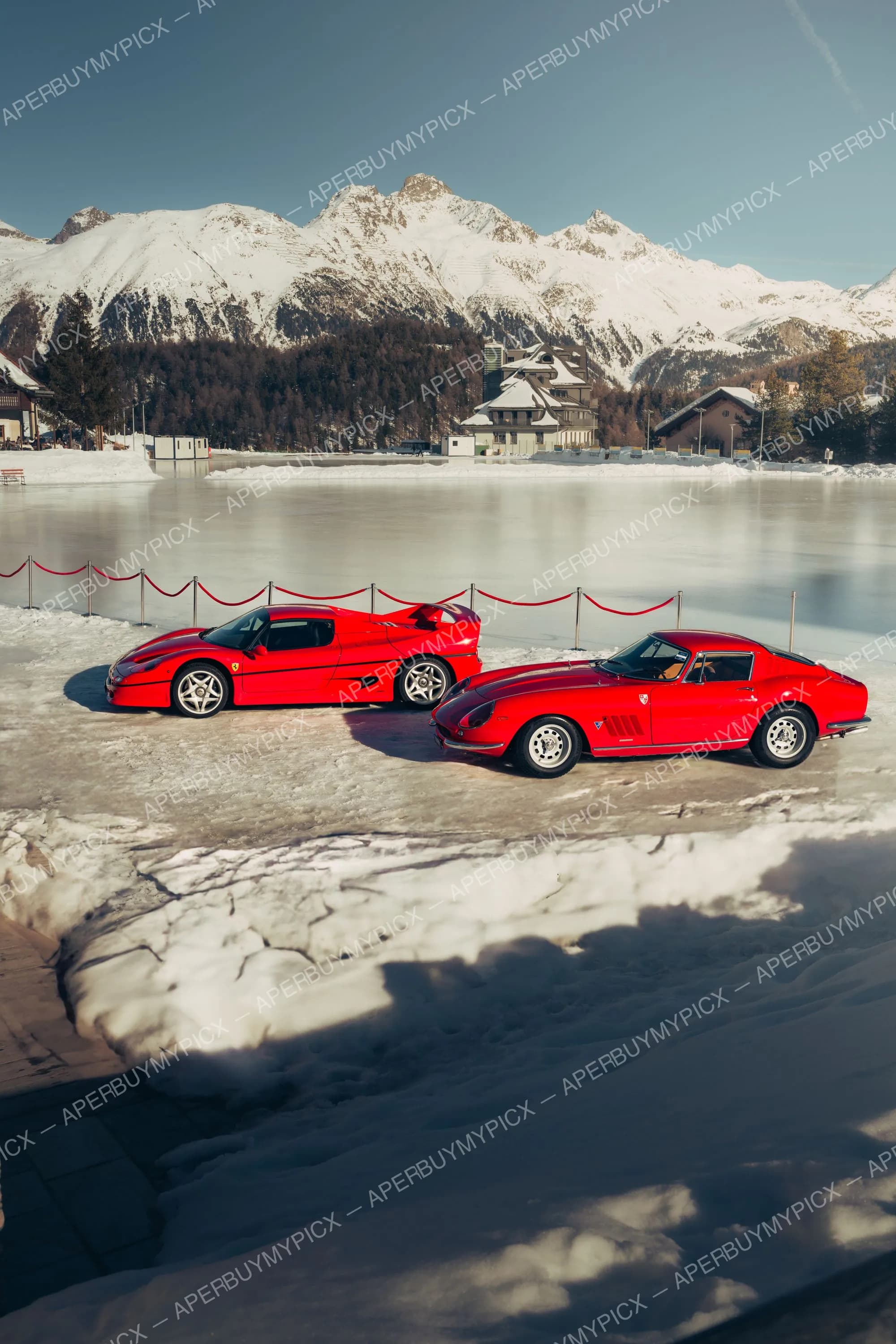 Deux Ferrari rouges, une F50 moderne et une 275 GTB classique, garées sur un lac gelé enneigé à St. Moritz avec montagnes enneigées et chalets en arrière-plan.