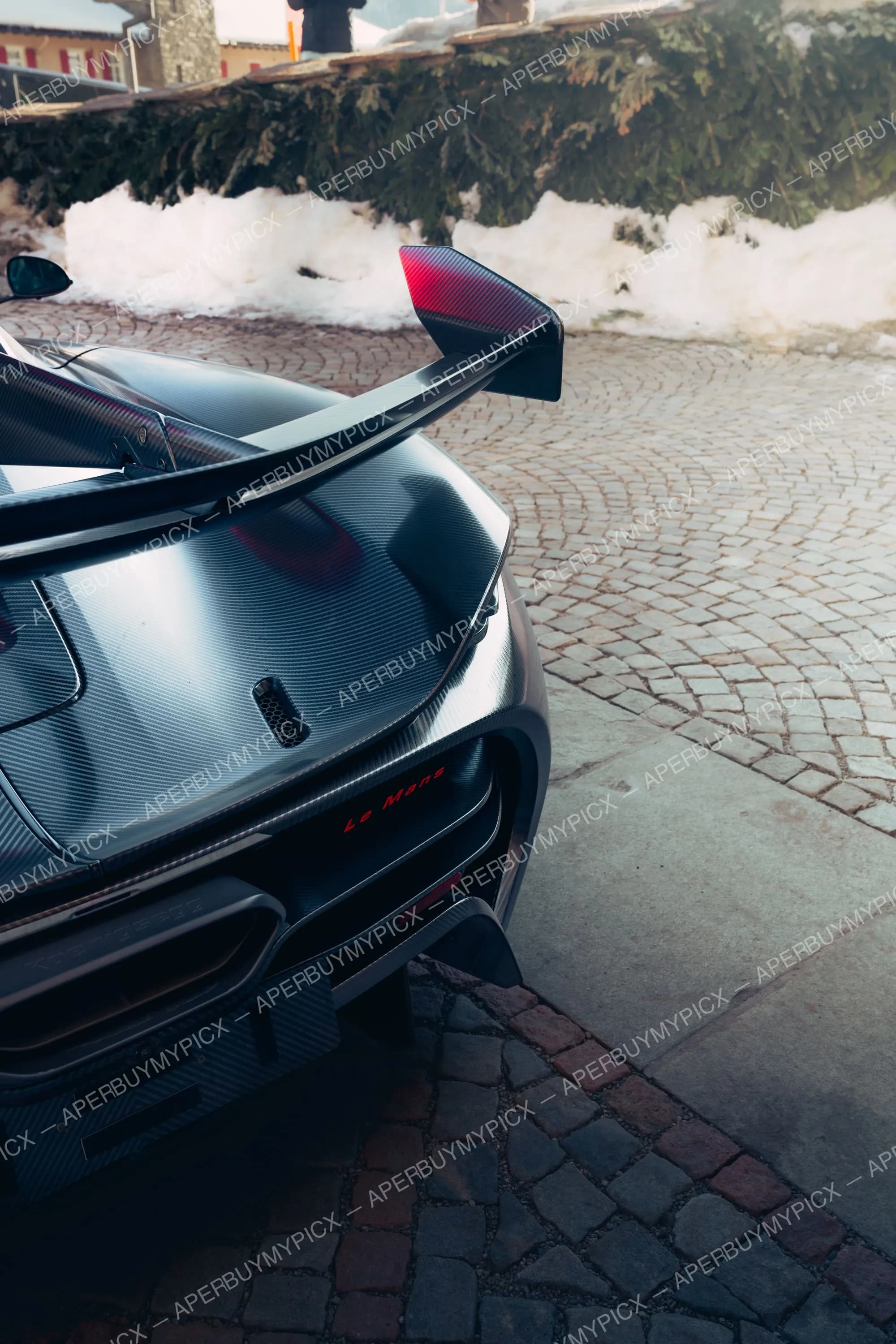 Vue arrière rapprochée d'une McLaren 675LT Le Mans en fibre de carbone avec aileron rouge et noir, garée sur des pavés enneigés à St. Moritz.