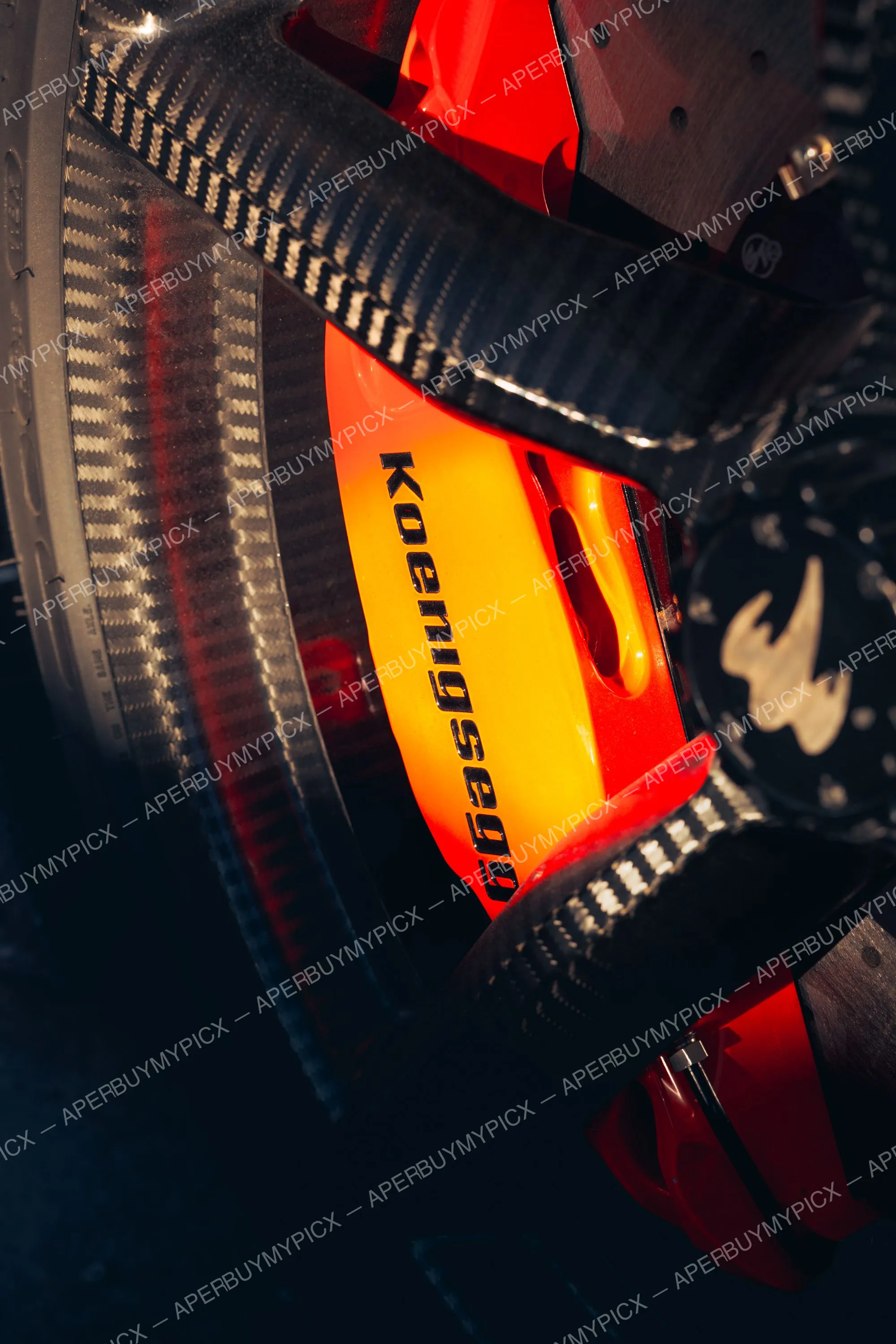 Gros plan d'un étrier de frein orange marqué Koenigsegg sur un disque de frein carbone-céramique, jante en fibre de carbone et pneu visibles au coucher du soleil