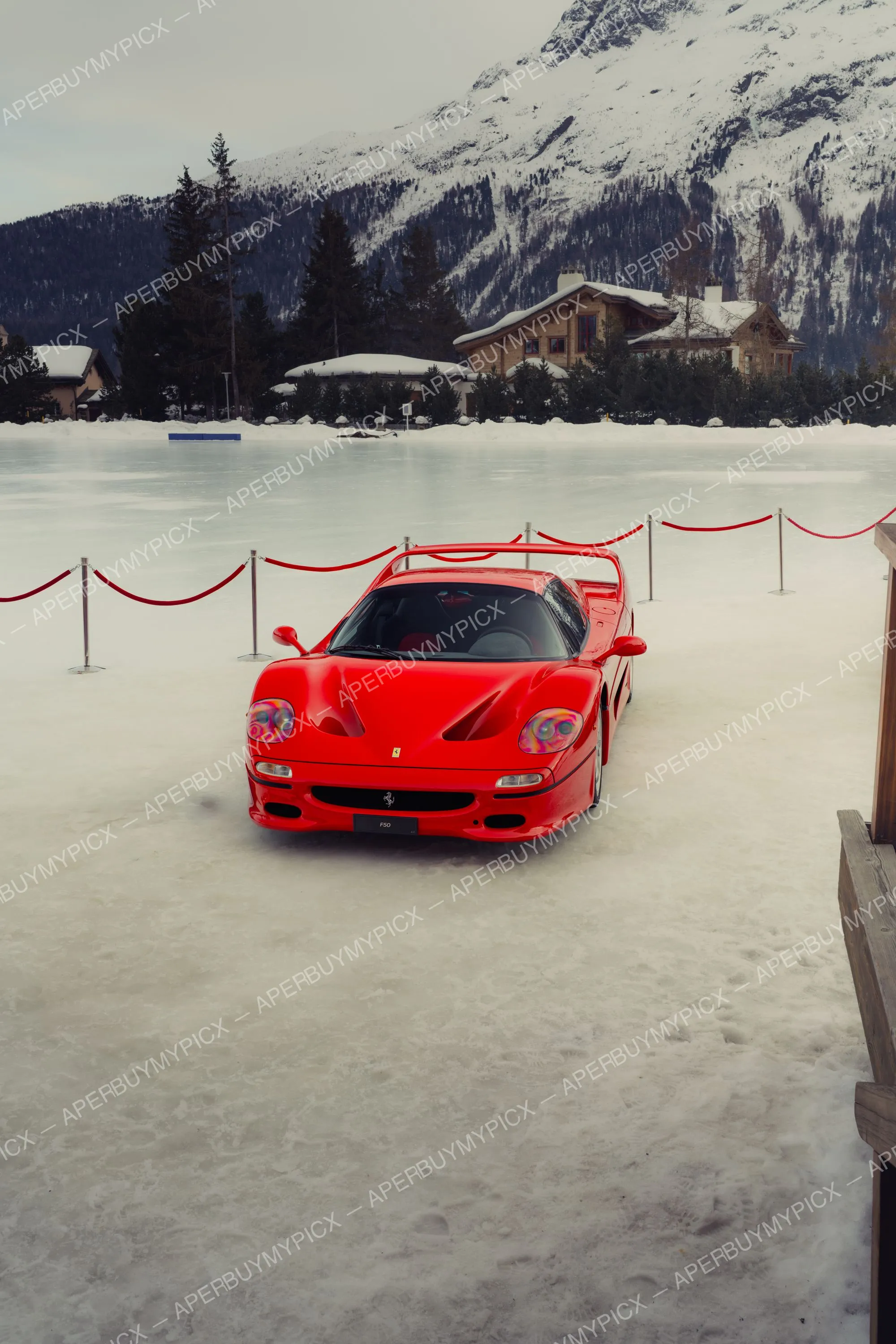 Ferrari F50 rouge garée sur un lac gelé enneigé à St. Moritz, entourée d'un cordon rouge, avec chalet et montagnes enneigées en arrière-plan