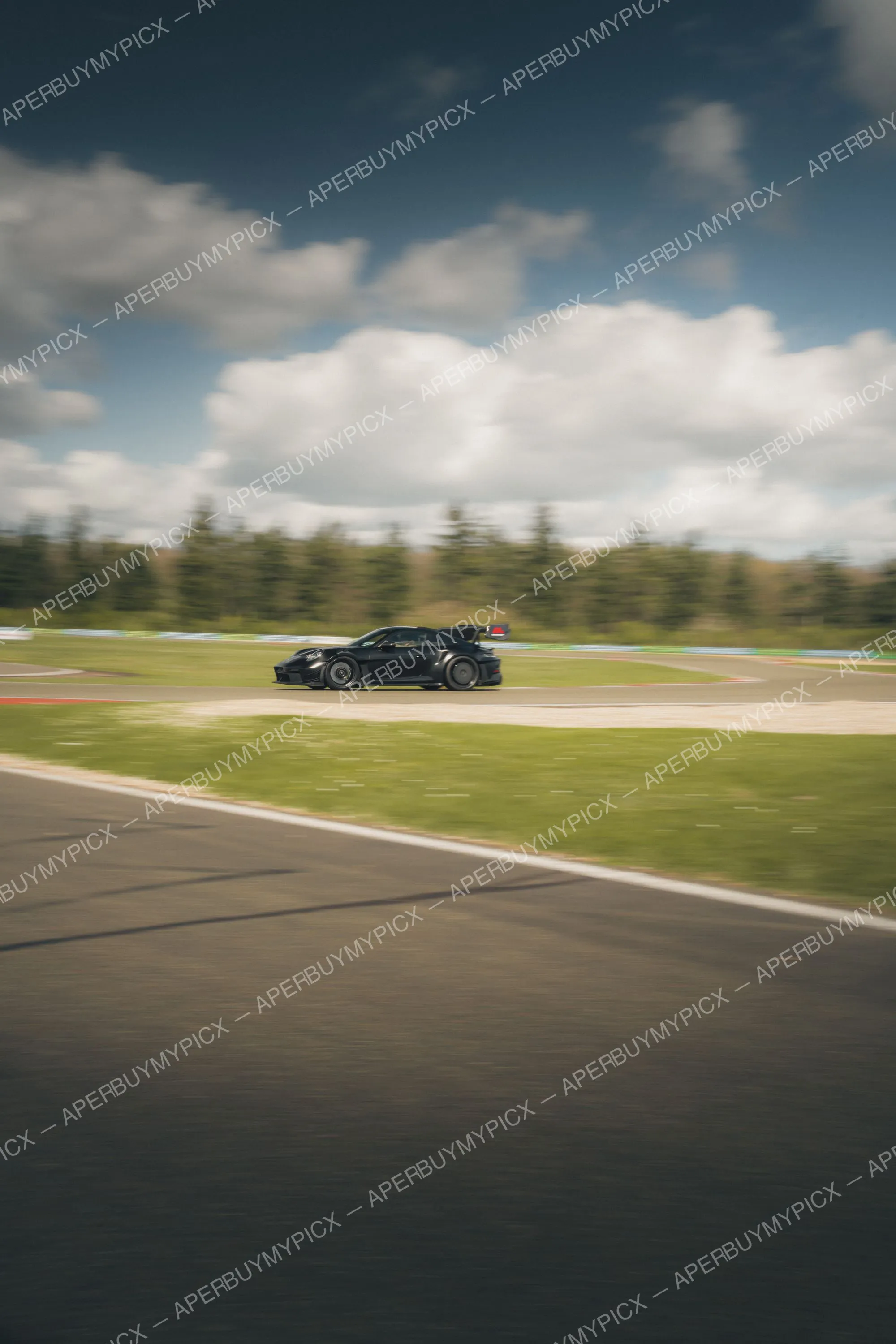 Porsche 911 GT3 RS noire en vitesse sur un circuit, effet de filé, ciel nuageux et arbres en arrière-plan