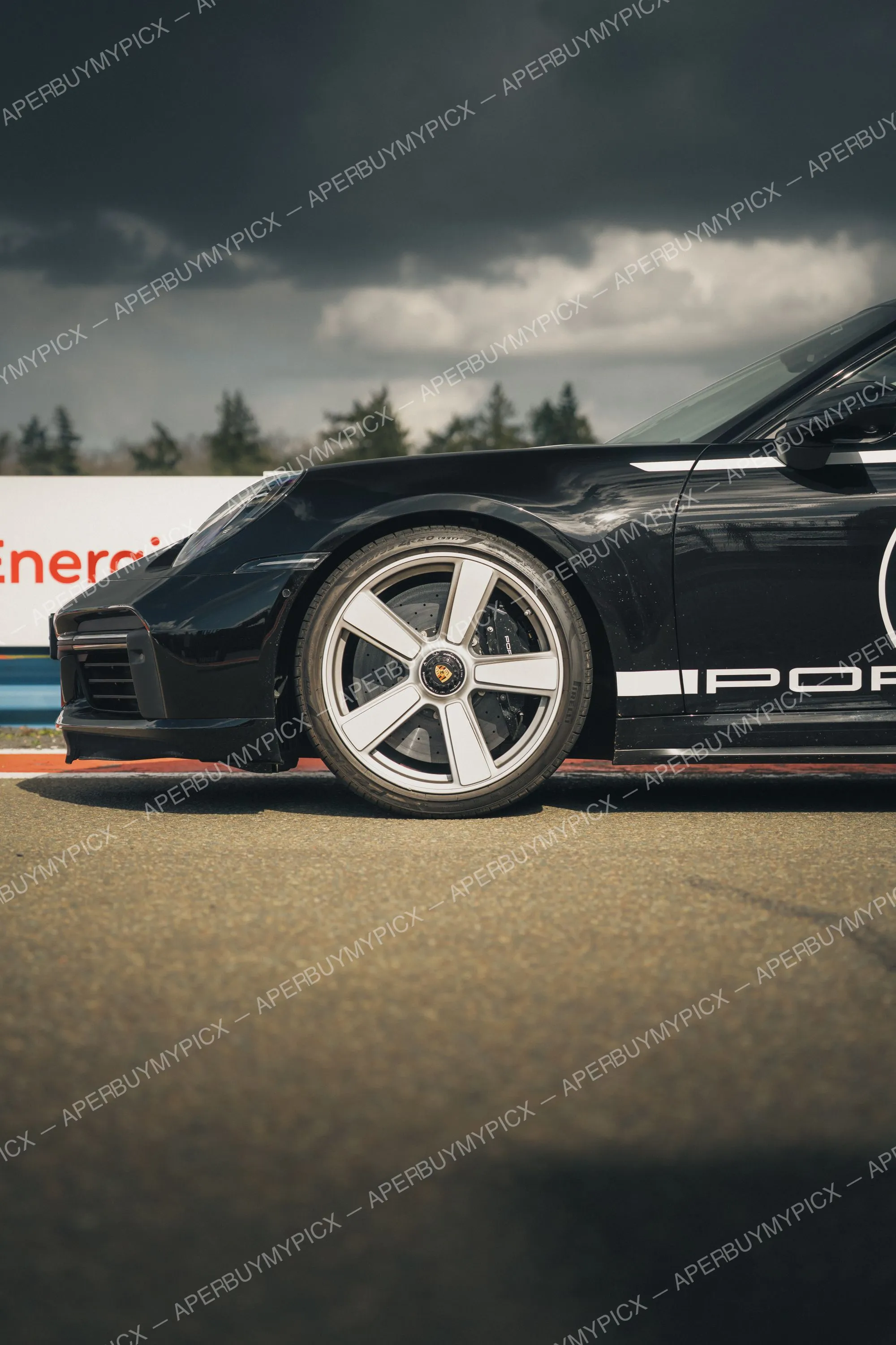 Porsche 911 noire vue de profil avant sur un circuit, jante argentée à cinq branches, ciel orageux et sombre en arrière-plan