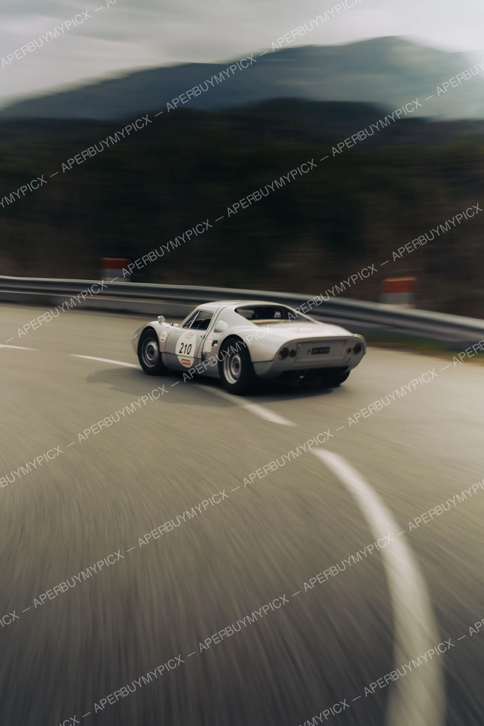 Porsche 904 GTS blanche numéro 210 filant sur une route sinueuse de montagne avec effet de vitesse, vue arrière, lors du Tour Auto 2025.